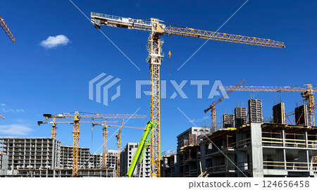 Tower cranes standing tall at a busy construction site against a clear blue sky. Multiple buildings in various stages of completion, modern architecture development Tower cranes standing tall at a busy construction site against a clear blue sky. Multiple buildings in various stages of completion, modern architecture development 124656458
