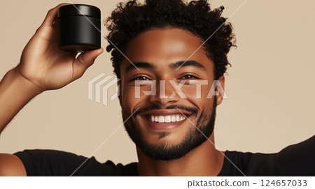 Male model with smiling expression holding black body balm in hand above head.  124657033