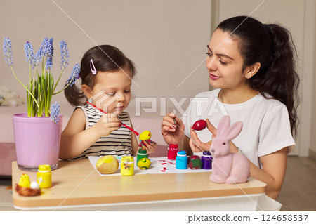 Happy mother and cute little child girl are preparing to celebrate Easter at home. Mom and daughter painting eggs before Easter together. 124658537