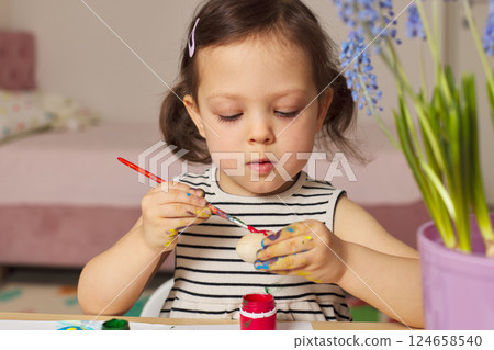 Little child girl paint Easter eggs at home. kid is preparing for Easter. 124658540
