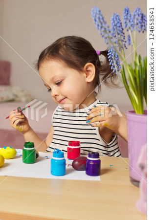 Little child girl paint Easter eggs at home. kid is preparing for Easter. 124658541