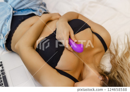Young woman holding sex toy dildo vibrator in bed Young woman holding sex toy dildo vibrator in bed 124658588