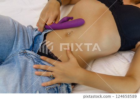 Woman in bed under sheets holding vibrator in hand Woman in bed under sheets holding vibrator in hand 124658589