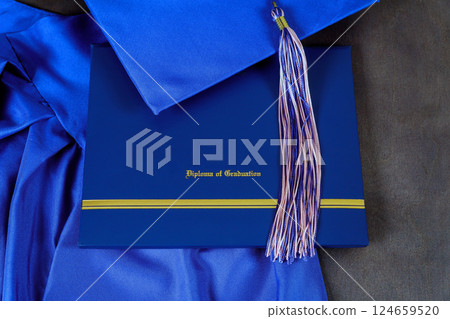 Blue graduation cap, diploma of graduation are arranged on gray surface showcasing academic achievement. Blue graduation cap, diploma of graduation are arranged on gray surface showcasing academic achievement. 124659520