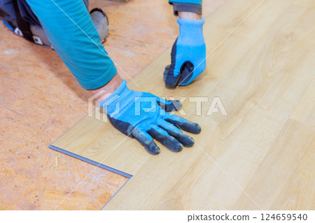 Skilled individual lays down laminate flooring planks, focused on achieving perfect alignment Skilled individual lays down laminate flooring planks, focused on achieving perfect alignment 124659540