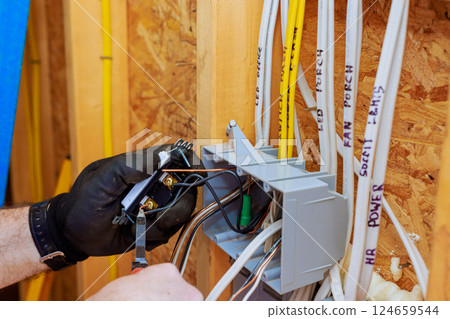 An electrician is connecting wires to switch light in junction box while preparing for electrical service installation 124659544