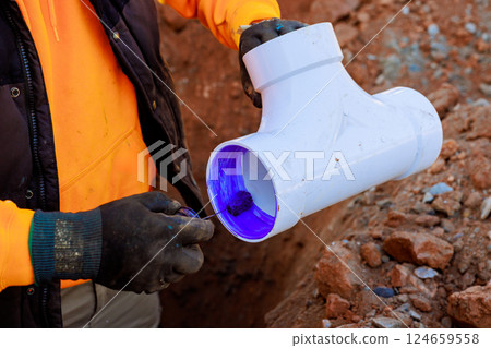 Construction worker is using adhesive on PVC pipe fitting at trench construction site Construction worker is using adhesive on PVC pipe fitting at trench construction site 124659558