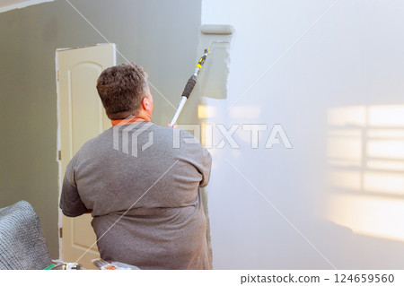 Paint worker painting wall gray over white in bright room, showing renovation in progress. Paint worker painting wall gray over white in bright room, showing renovation in progress. 124659560