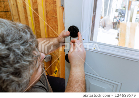 Handyman carefully installs door handle in house under renovation, focusing on details of door fixture. Handyman carefully installs door handle in house under renovation, focusing on details of door fixture. 124659579