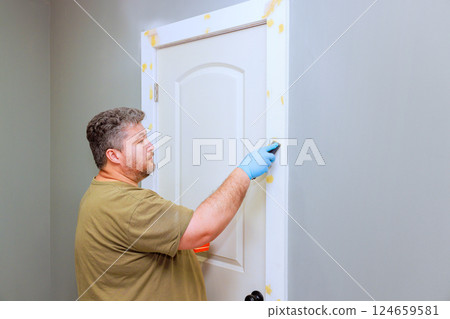 Handyman is carefully touching up using wood filler door frame with applies wood filler in well lit room Handyman is carefully touching up using wood filler door frame with applies wood filler in well lit room 124659581