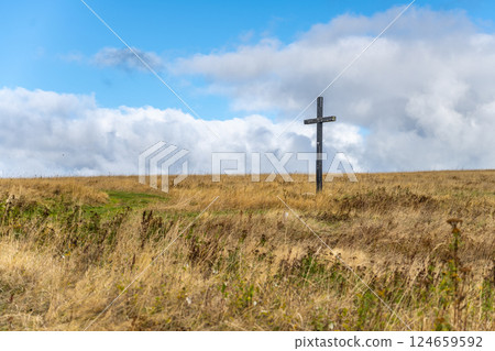 A wooden cross is positioned prominently on a mountain meadow near Haj in the Ore Mountains of Czechia, surrounded by tall grasses and vivid skies, creating a serene atmosphere. 124659592