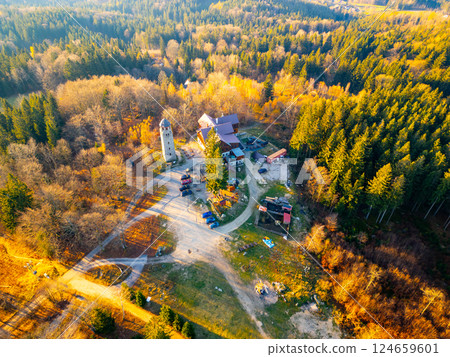 A sunny autumn morning at the Bramberk lookout tower in the Jizera Mountains reveals vibrant foliage and a scenic hut surrounded by lush trees, inviting visitors to enjoy nature's beauty. 124659601
