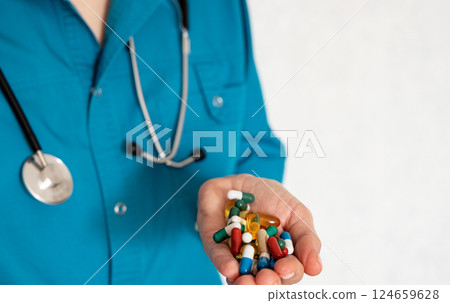 Health professional holds various pills and capsules while wearing a stethoscope 124659628