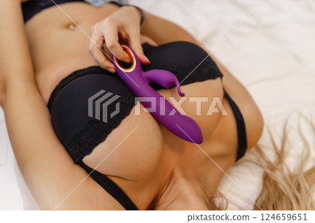Woman in bed under sheets holding vibrator in hand 124659651
