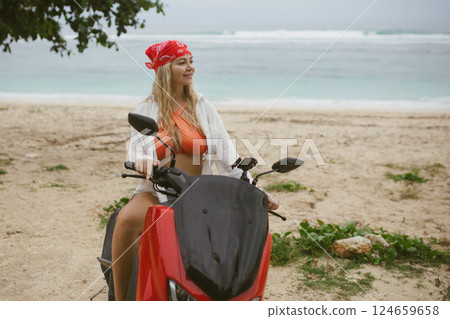 Attractive caucasian woman in a bikini swimsuit and on a bike scooter near the beach in sunny weather. 124659658