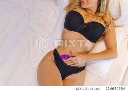 Young woman holding sex toy dildo vibrator in bed Young woman holding sex toy dildo vibrator in bed 124659664
