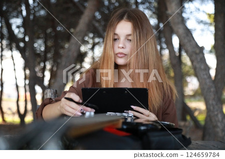 Girl Writes Music Notes On Sheet Music Sitting At The Park Table In The Nature 124659784