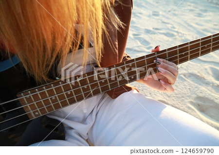 Girl Plays The Bass Instrument Sitting On The Beach At Sunset Near The Ocean Girl Plays The Bass Instrument Sitting On The Beach At Sunset Near The Ocean 124659790