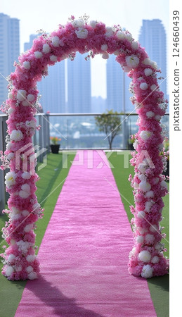 A pink flower archway with a pink carpet leads to a cityscape view, perfect for a wedding or special event 124660439