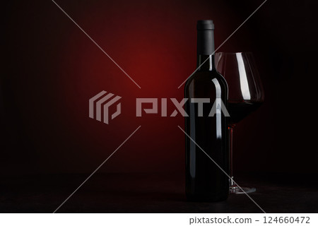 Bottle of red wine and wineglass on dark red background. Front view 124660472