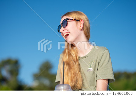 Young woman in sunglasses enjoying refreshing drink against blue sky. 124661063