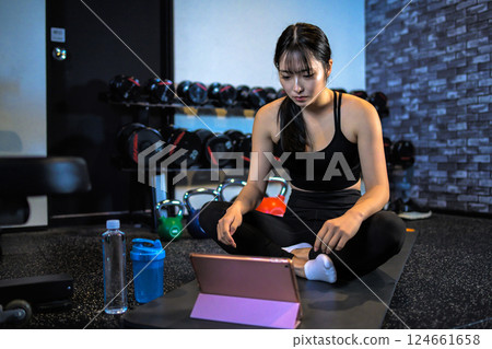 A cool woman exercising at the gym while watching YouTube videos on a tablet Stretching How to do it Video viewing A cool woman exercising at the gym while watching YouTube videos on a tablet Stretching How to do it Video viewing 124661658