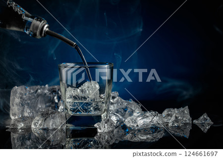 Crystal clear vodka or gin being poured over ice in a glass. 124661697