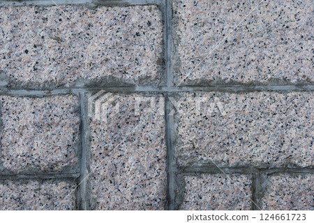 a textured stone wall made of large granite blocks. The surface displays mix of pink and gray hues, with visible flecks and patterns typical of granite. The mortar space between stones is neatly apply 124661723