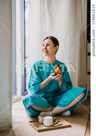 Young woman sitting on the floor holding a lit amber glass candle beside a tray with incense and tea. Spiritual minimalism at home, quiet luxury, cozy meditation, sacred simplicity Young woman sitting on the floor holding a lit amber glass candle beside a tray with incense and tea. Spiritual minimalism at home, quiet luxury, cozy meditation, sacred simplicity 124661814