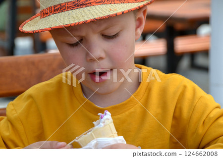 Close up image of boy hand holding fresh waffle cone with vanilla and raspberry ice cream on the wooden background. Walking. Outdoors. High quality photo. High quality photo 124662008