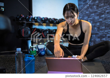 一位酷酷的女性在健身房鍛煉身體,同時在平板電腦上觀看 YouTube 視頻 伸展運動 如何做 觀看視頻 一位酷酷的女性在健身房鍛煉身體,同時在平板電腦上觀看 YouTube 視頻 伸展運動 如何做 觀看視頻 124662657