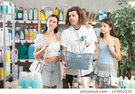 Family with full basket choosing something in supermarket Family with full basket choosing something in supermarket 124662830