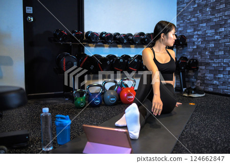 A cool woman exercising at the gym while watching YouTube videos on a tablet Stretching How to do it Video viewing 124662847