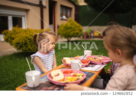 Children enjoy a sunny breakfast in a lush garden setting Children enjoy a sunny breakfast in a lush garden setting 124662852