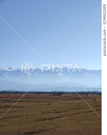 A peaceful rural field stretches toward a distant mountain range covered in snow. The clear sky and soft light enhance the calmness of the scene. 124662889