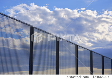 High security fence reflecting clouds and blue sky High security fence reflecting clouds and blue sky 124663003