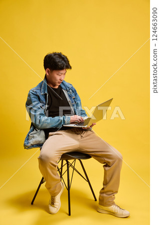 Focused young man using laptop while sitting on chair in studio, working with intention. Concept of business, remote work 124663090