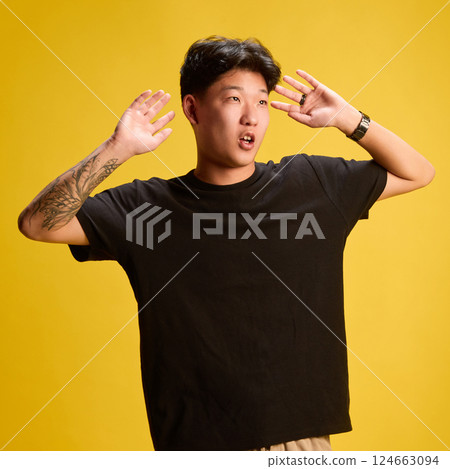 Expressive young man gesturing with both hands near face as if surprised or impressed, yellow backdrop. Expressive young man gesturing with both hands near face as if surprised or impressed, yellow backdrop. 124663094
