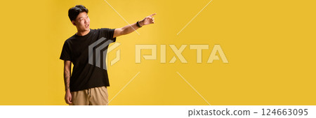 Energetic young man in casual outfit pointing away with excitement against yellow backdrop. Concept of holiday vibe. Energetic young man in casual outfit pointing away with excitement against yellow backdrop. Concept of holiday vibe. 124663095