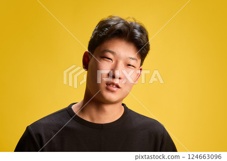 Smiling young man tilting head slightly with confident attitude against warm yellow backdrop. Concept of self-expression 124663096