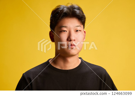 Close-up of serious young man in black t-shirt looking directly into camera against vivid yellow background. Concept of emotion, Close-up of serious young man in black t-shirt looking directly into camera against vivid yellow background. Concept of emotion, 124663099