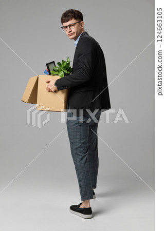 Stylish man in business suit walking away holding office box, turning back with suspicious expression. Concept of office, career tension Stylish man in business suit walking away holding office box, turning back with suspicious expression. Concept of office, career tension 124663105