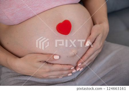 Caucasian pregnant woman holding heart on belly background. Third trimester. Caucasian pregnant woman holding heart on belly background. Third trimester. 124663161