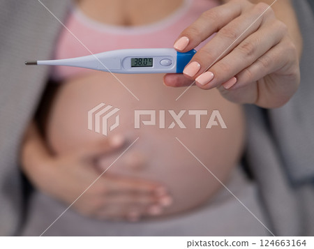 Pregnant woman measures temperature while sitting on the couch. Close up of the belly. Pregnant woman measures temperature while sitting on the couch. Close up of the belly. 124663164