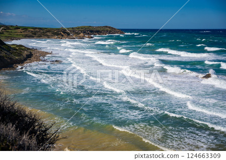A wild beach with a rugged rocky coastline and powerful waves crashing against the shore in Northern Cyprus. Raw energy of nature and the untamed beauty of the Mediterranean Sea 124663309