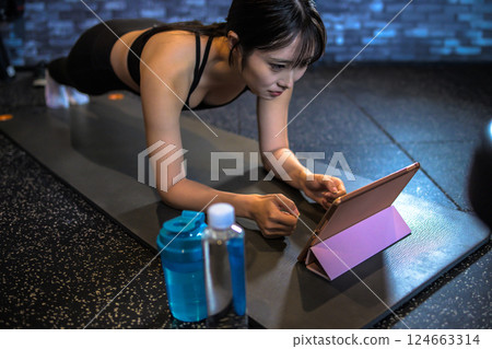一名女子一邊做平板撐一邊觀看影片 一名酷炫女子在健身房鍛煉 124663314