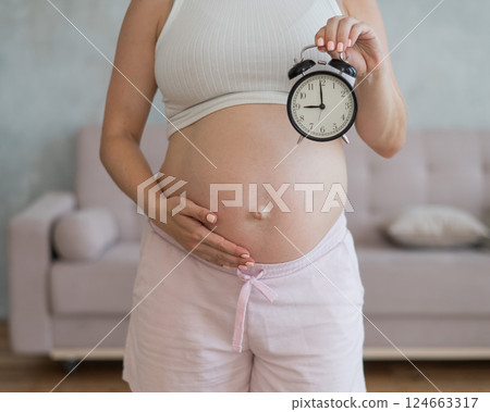 Close up of pregnant woman's belly holding alarm clock. Close up of pregnant woman's belly holding alarm clock. 124663317