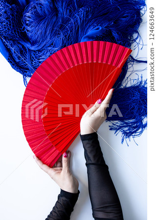 Female hands holding red fan with blue shawl background 124663649