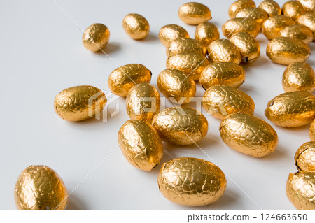 Golden foil wrapped chocolate eggs on white surface 124663650