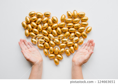 Heart shaped arrangement of gold wrapped chocolate eggs with caucasian child hands 124663651